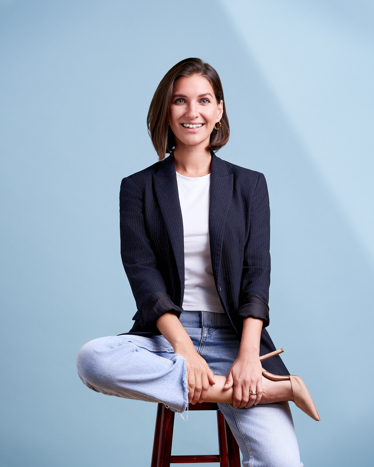 Lächelnde Frau in schwarzem Blazer im Schneidersitz auf einem Hocker, Business Casual Frankfurt