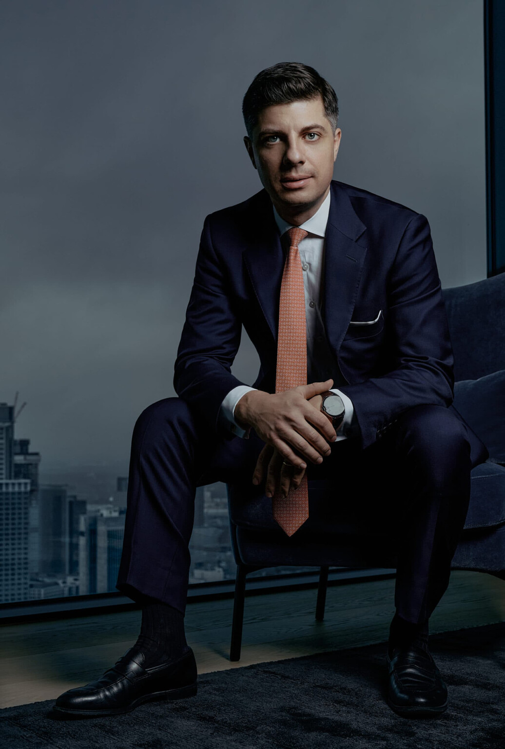 Corporate Fotografie Frankfurt: Mann im Anzug mit orangefarbener Krawatte vor Fenster mit Stadtblick