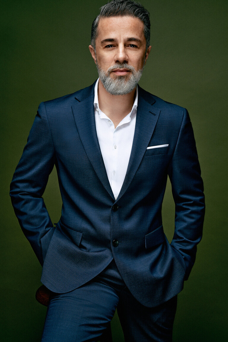 Business Portrait eines Mannes im blauen Anzug mit beiden Händen in den Hosentaschen vor grünem Hintergrund
