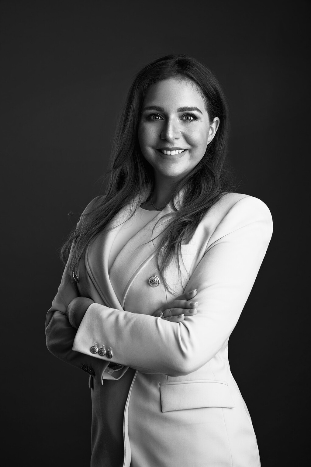 Schwarzweiß Business Portrait einer lächelnden Frau im hellen Blazer mit verschränkten Armen, Frankfurt