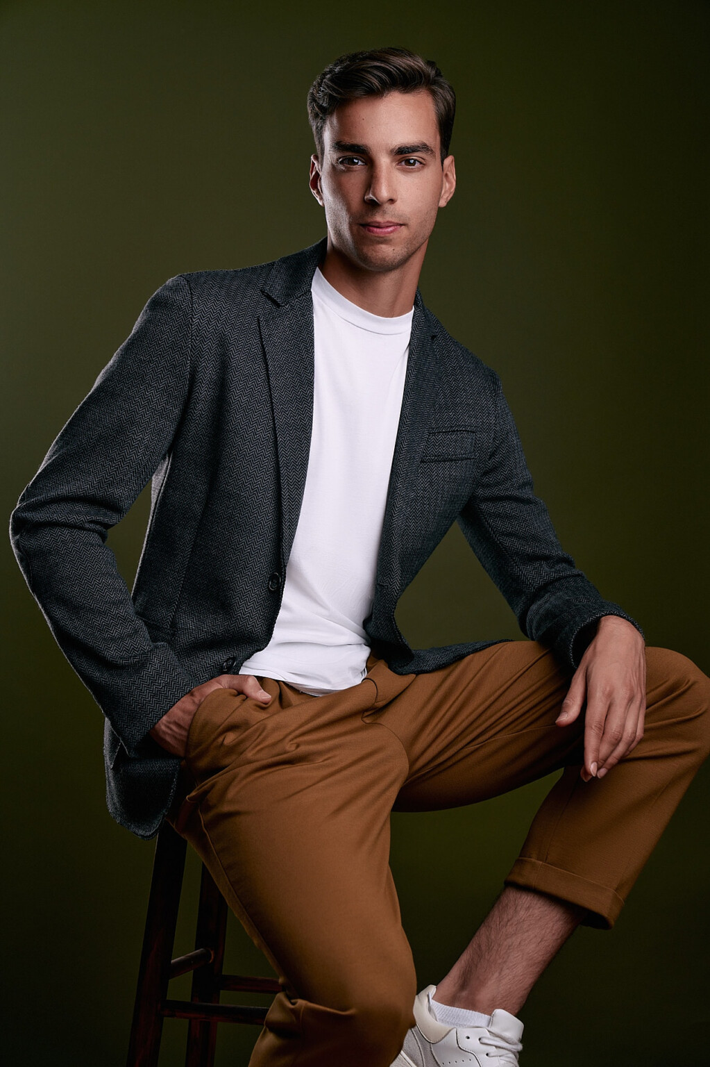 Mann im grauen Blazer mit weißem T-Shirt auf einem Hocker vor grünem Hintergrund, Business Casual Frankfurt