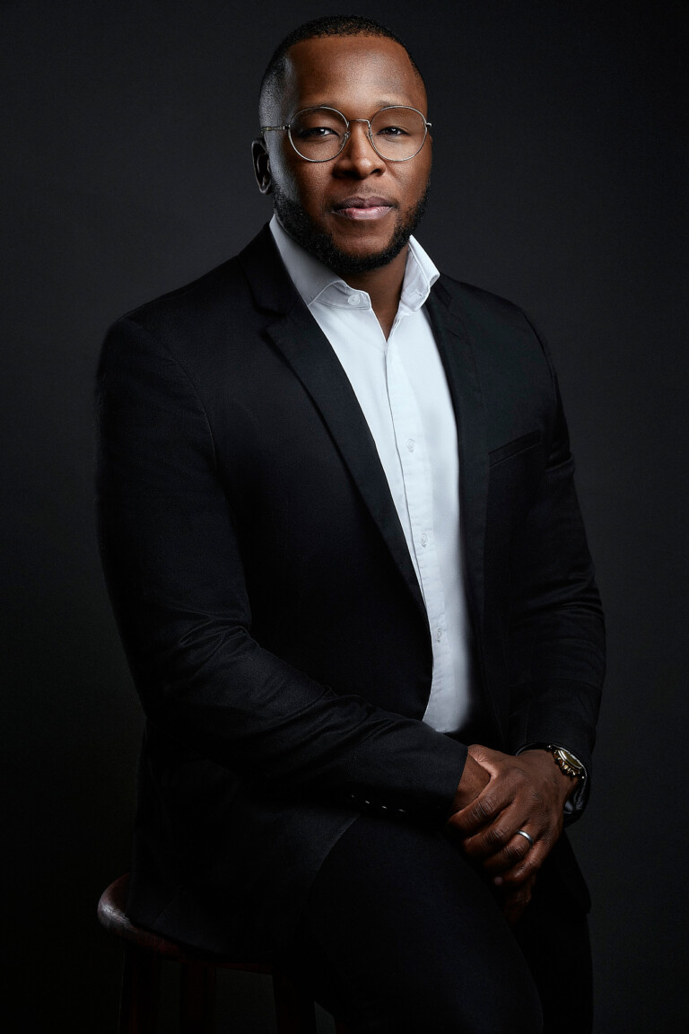 Home 8 Mann mit Brille in schwarzem Anzug auf einem Hocker, Business Portrait im Fotostudio Frankfurt