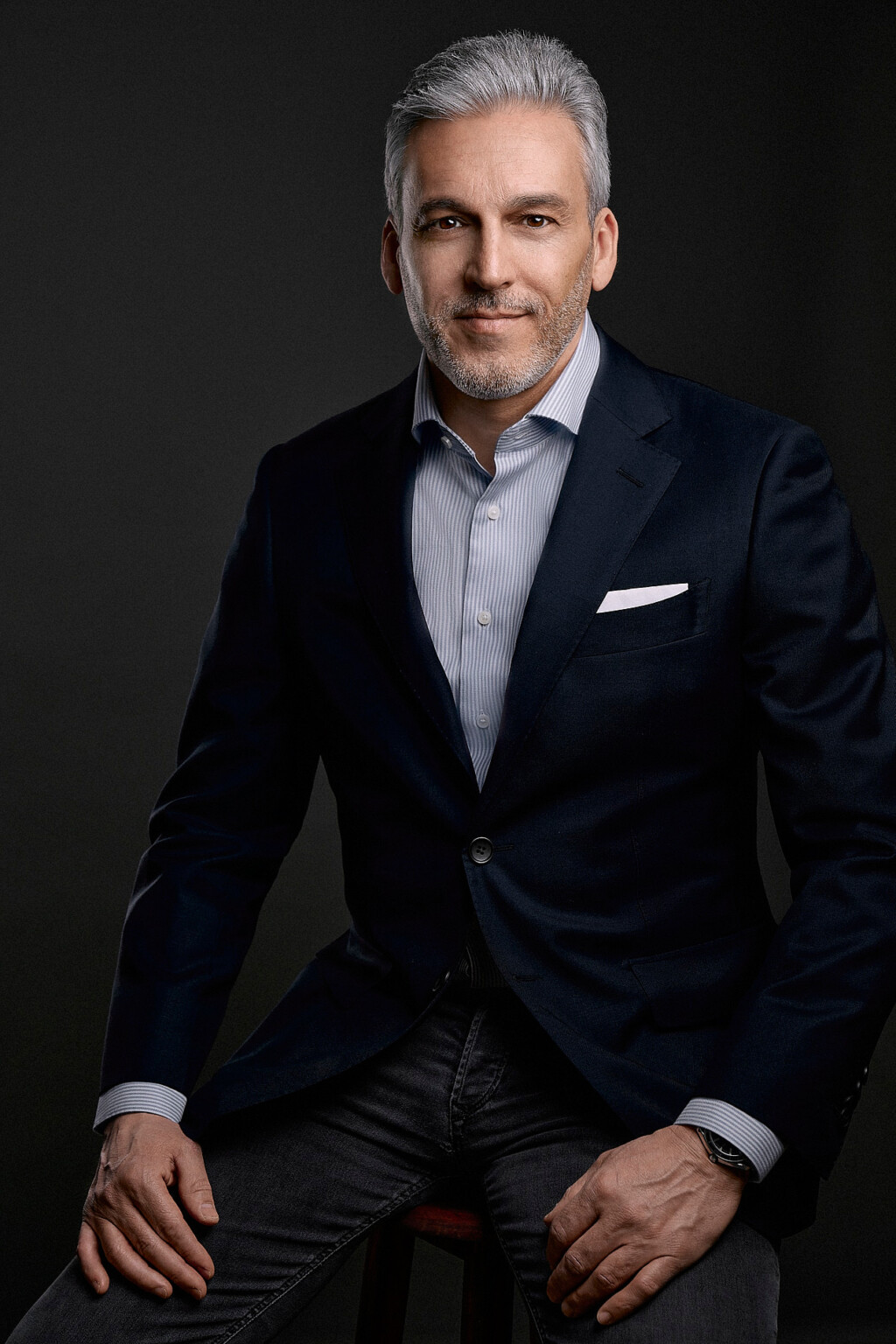 Seated man with a grey beard in a dark jacket with pocket square, business portrait Frankfurt