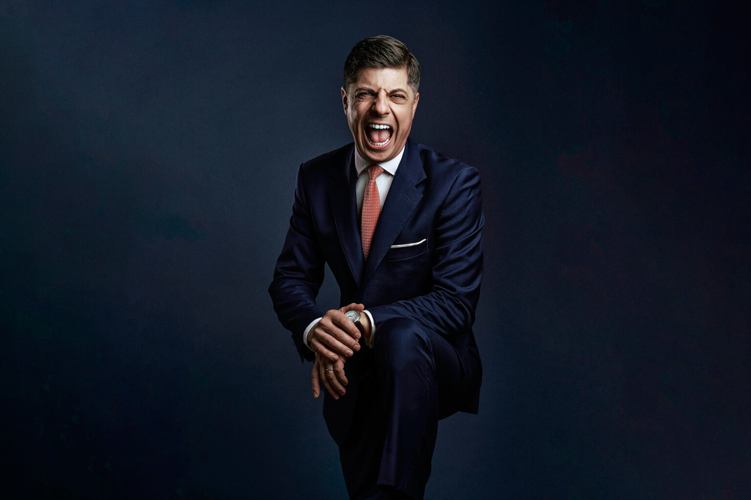 Lachender Mann in Anzug mit roter Krawatte auf einem Hocker, natürliches Business Portrait Frankfurt