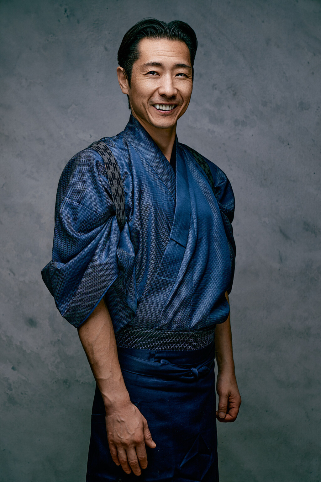 Lachender Mann in traditioneller blauer Kleidung vor grauem Hintergrund, Portrait Arthouse Studio Frankfurt