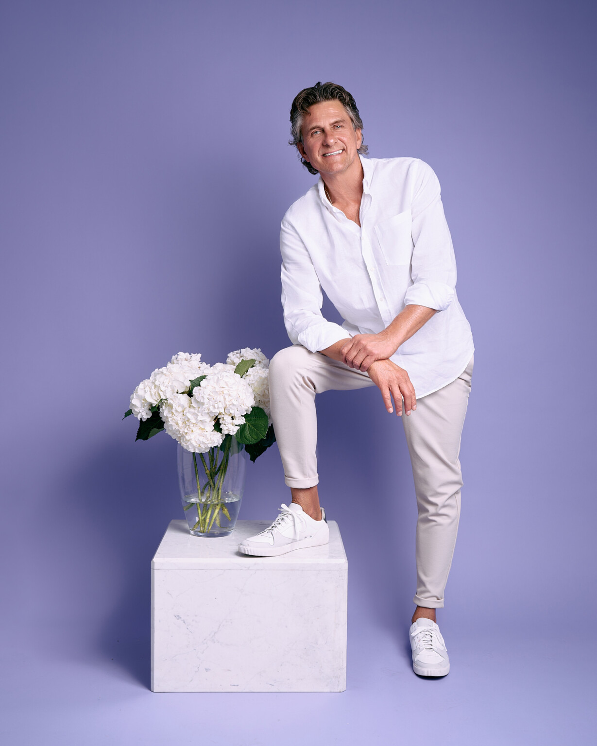 Lächelnder Mann in weißem Hemd am Marmorsockel mit weißen Blumen vor Violett, Portrait Frankfurt