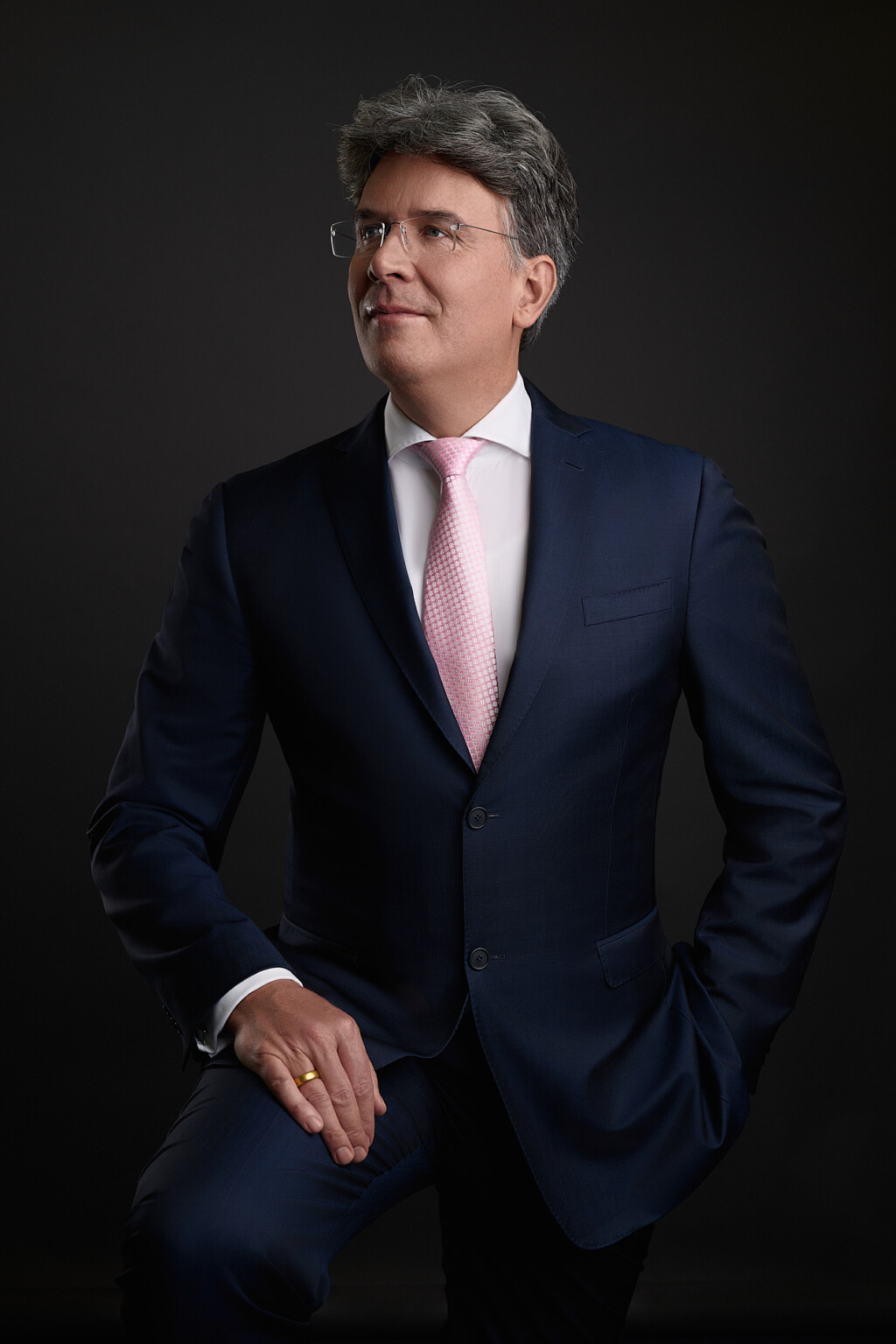 Mann im dunklen Anzug mit rosa Krawatte vor dunklem Hintergrund, Executive Portrait