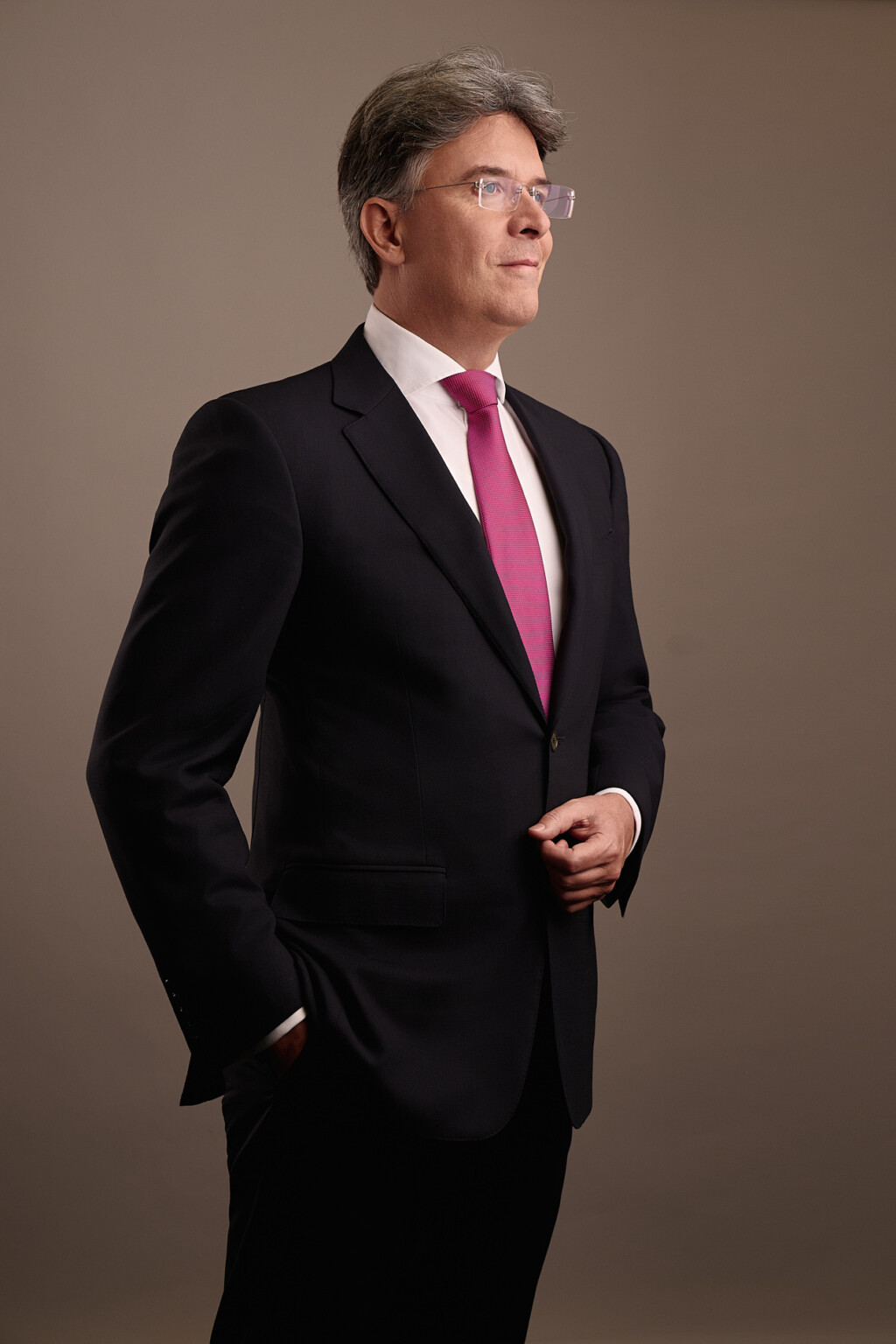Mann in dunklem Anzug mit rosa Krawatte vor warmem Hintergrund, Executive Portrait