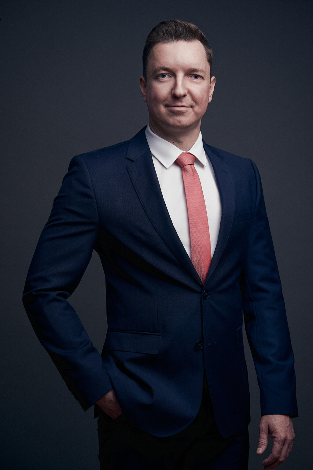 Lächelnder Mann in dunkelblauem Anzug mit roter Krawatte vor dunklem Hintergrund, Business Portrait