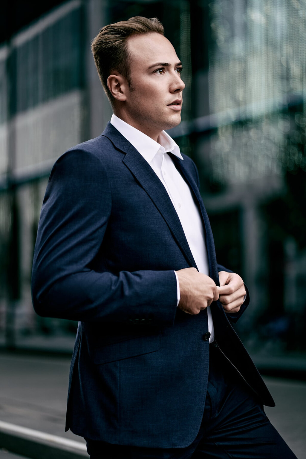 Mann im blauen Anzug vor einer Glasfassade in der Stadt, Business Portrait unter freiem Himmel