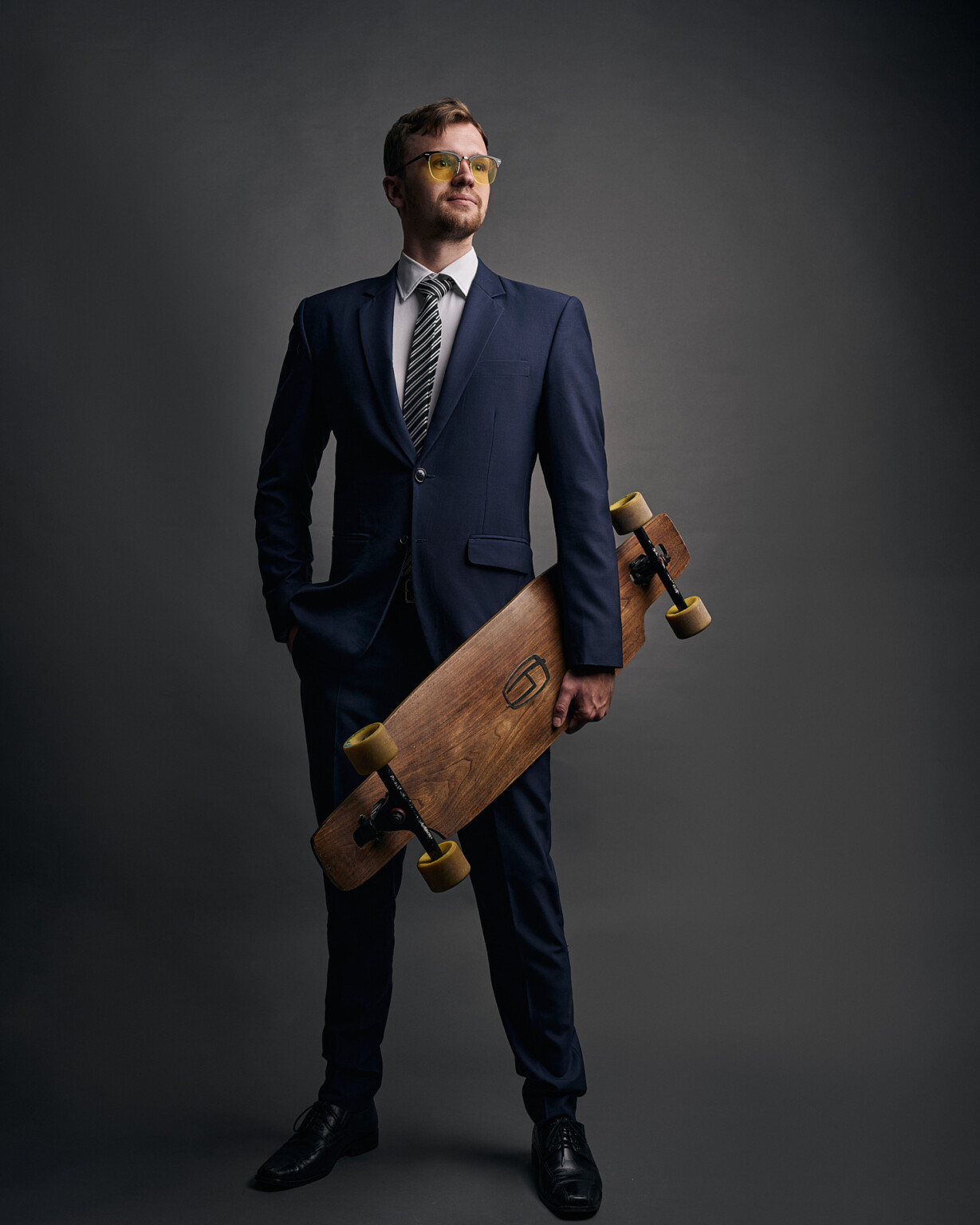 Mann in Anzug und Krawatte mit Longboard vor dunklem Hintergrund, Business Casual Frankfurt