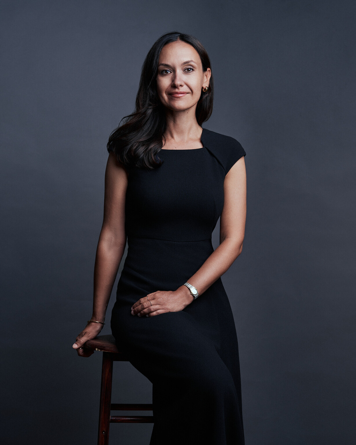Frau im schwarzen Kleid auf einem Hocker vor dunkelgrauem Hintergrund, Business Portrait Frankfurt