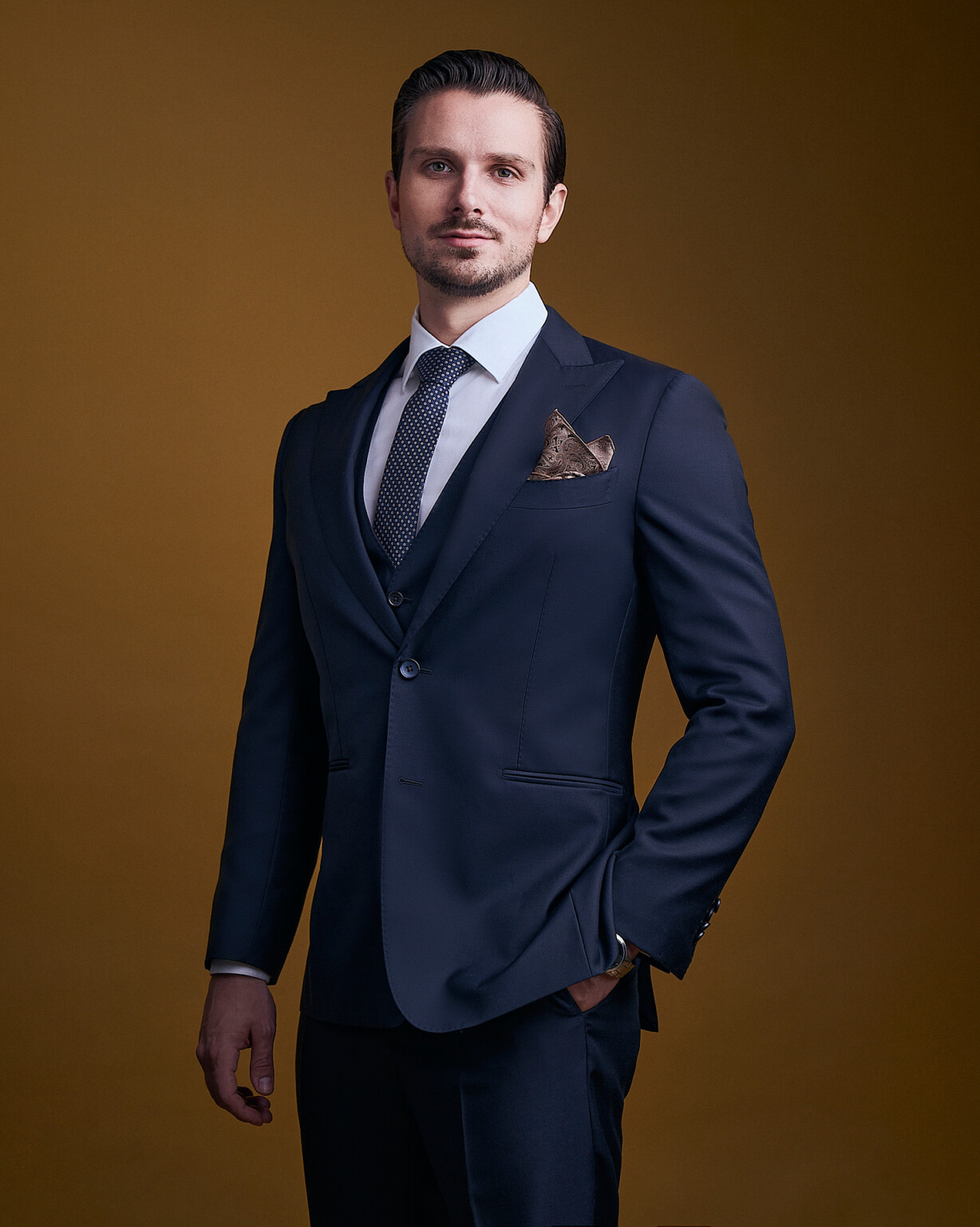 Mann in dunkelblauem Anzug mit Einstecktuch vor warmem braunem Hintergrund, Executive Portrait