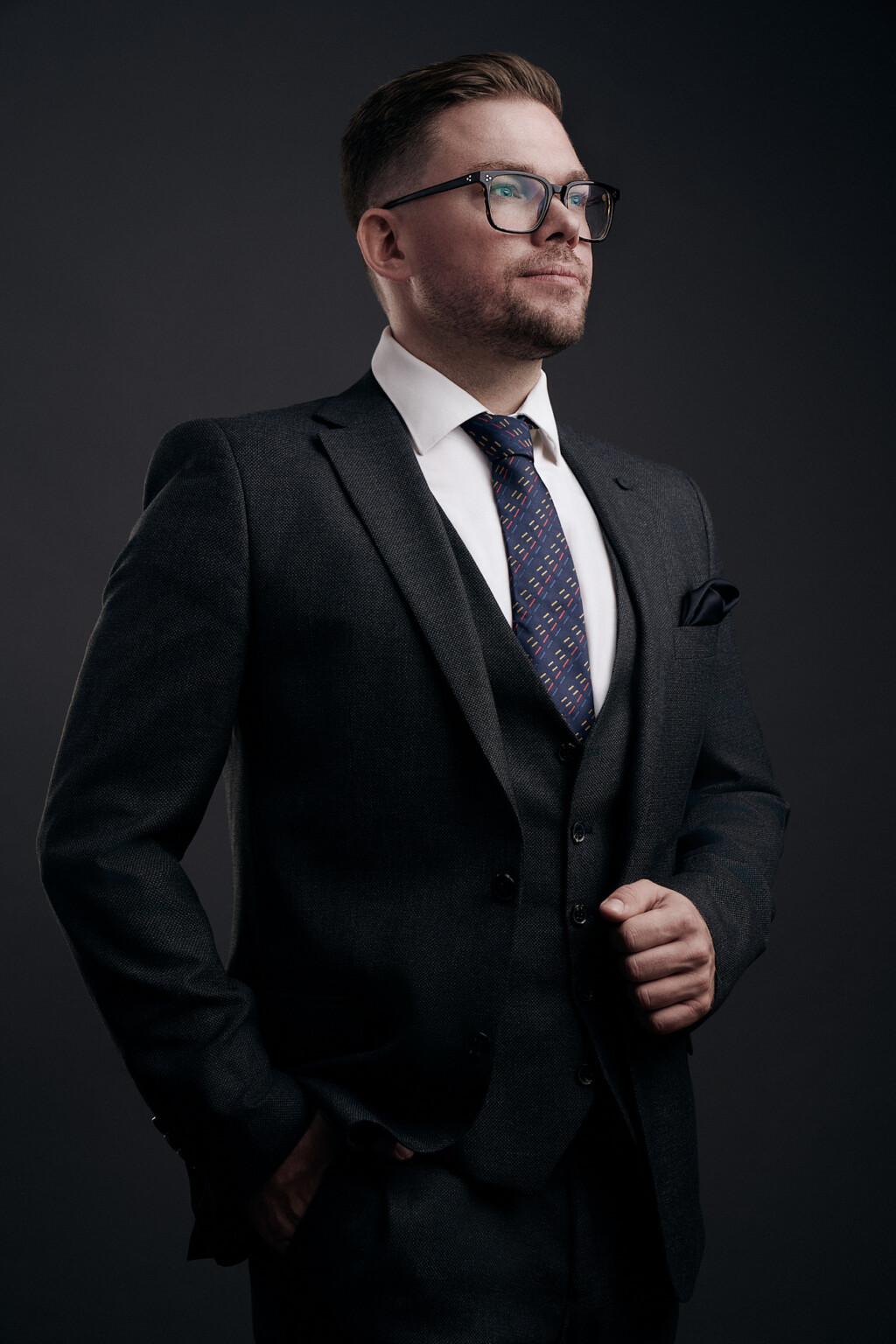 Mann mit Brille in dunklem Anzug, weißem Hemd und gemusterter Krawatte, Mitarbeiterportrait