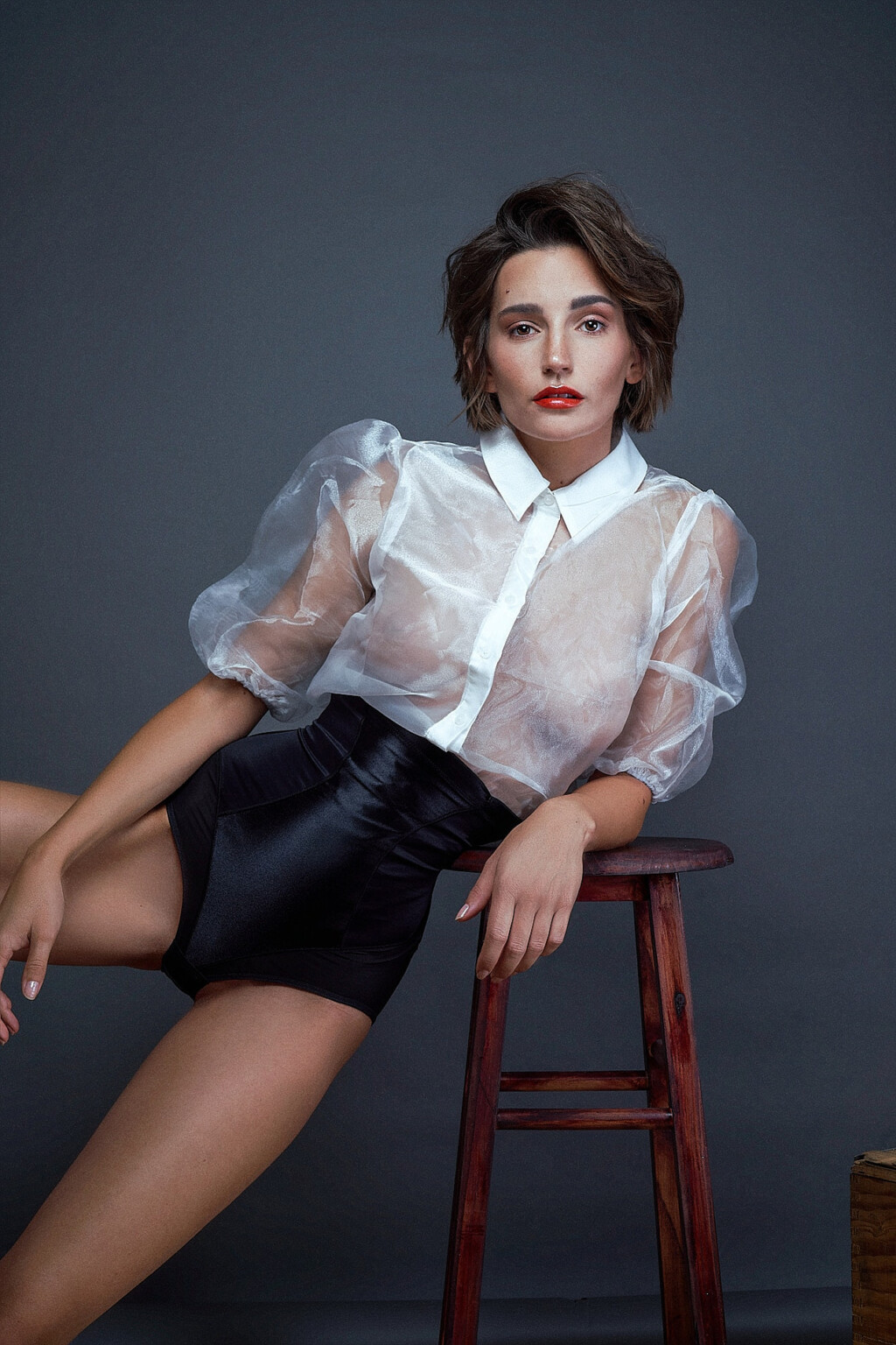 Janina Schiedlofsky in Organza-Bluse und schwarzer Shorts am Holzhocker