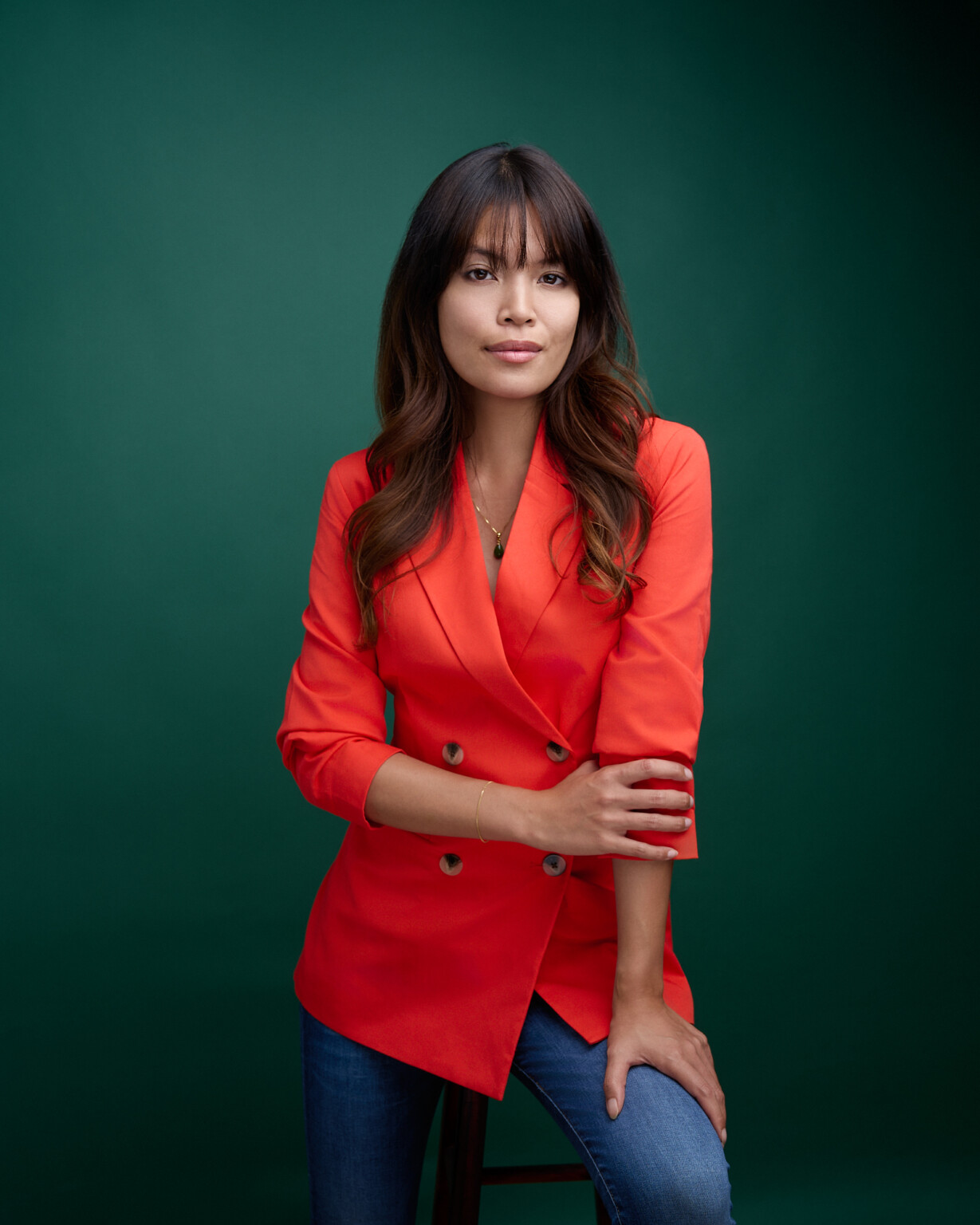 Frau im orangefarbenen Blazer mit Jeans auf einem Hocker, Business Casual Portrait Frau Frankfurt
