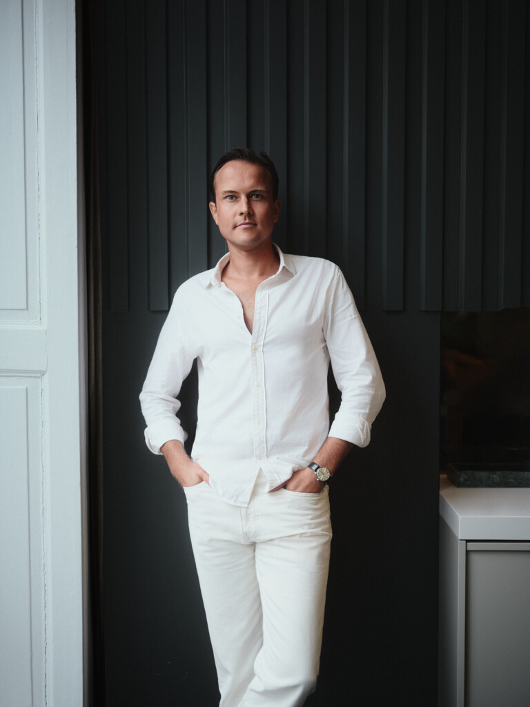 Home 12 Mann ganz in Weiß vor dunkler Lamellenwand, Business Casual Portrait