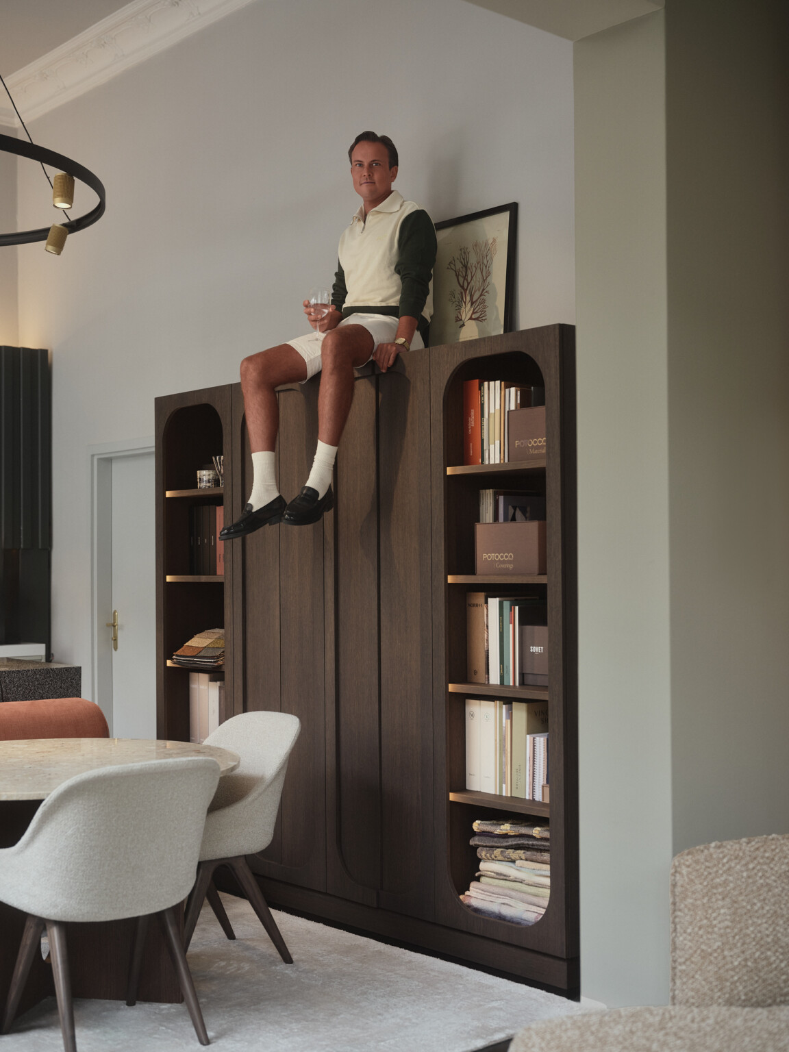 Mann sitzt lässig auf einem hohen Bücherschrank in einem hellen Wohnraum