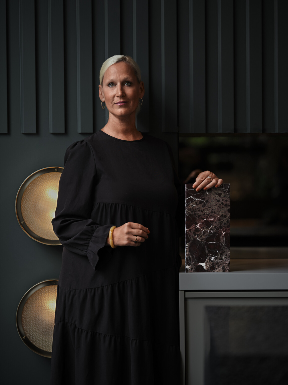 Business Portrait einer Frau mit kurzen blonden Haaren im schwarzen Kleid vor dunkler Wand