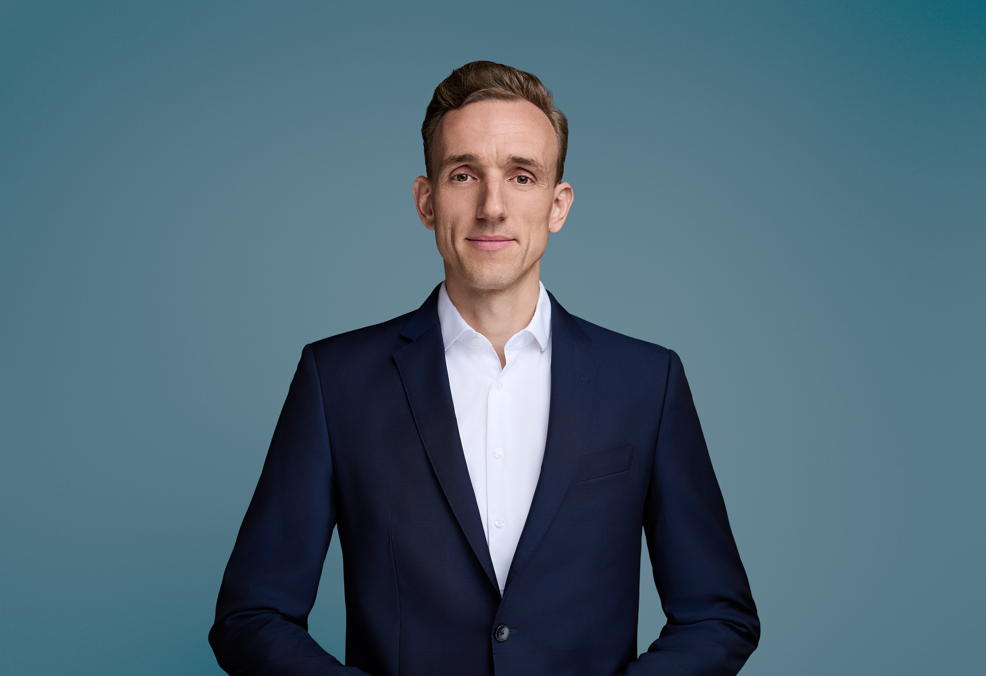 Business Portrait eines Mannes in dunkelblauem Sakko und weißem Hemd vor petrolfarbenem Hintergrund, Frankfurt
