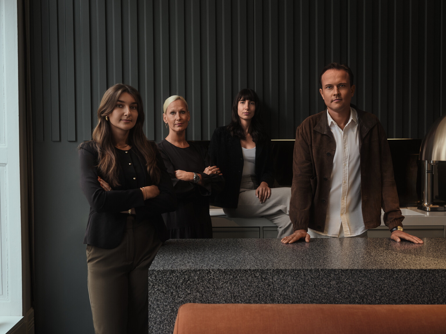Teamfoto von vier Personen an einer Granit-Kücheninsel in einem dunklen Showroom