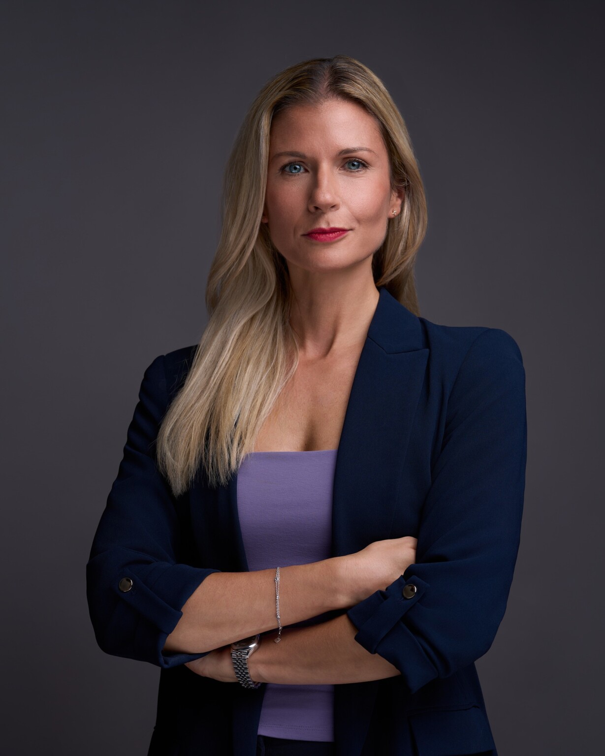 Business Portrait einer Frau im dunklen Blazer mit verschränkten Armen vor grauem Hintergrund, Executive Portrait