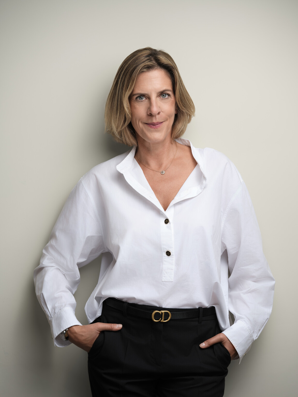 Lächelnde Frau in weißer Bluse, Hände in den Taschen, vor heller Wand, Business Portrait Frankfurt